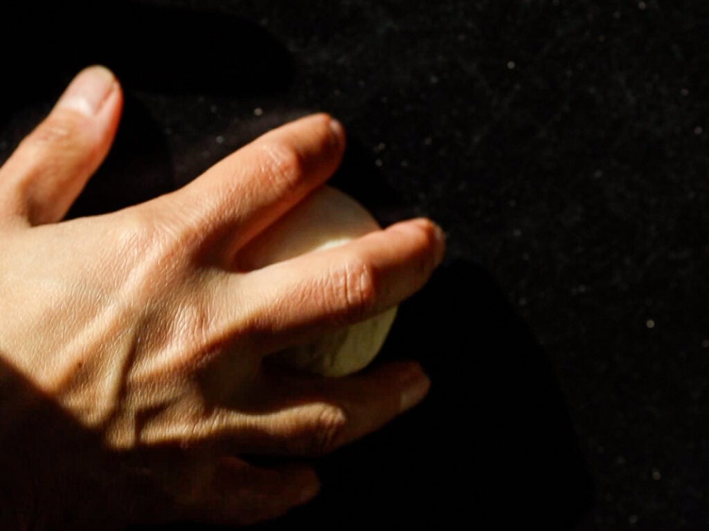 A hand kneading a small ball of dough on a dark surface, with sunlight casting shadows on the fingers.